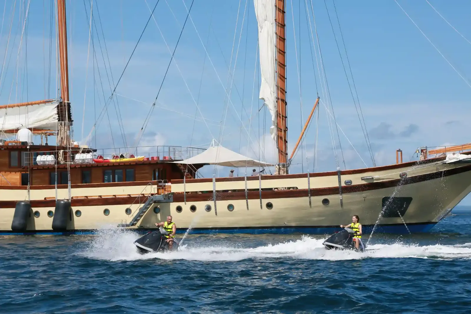 A luxury phinisi at anchor with jet skis alongside