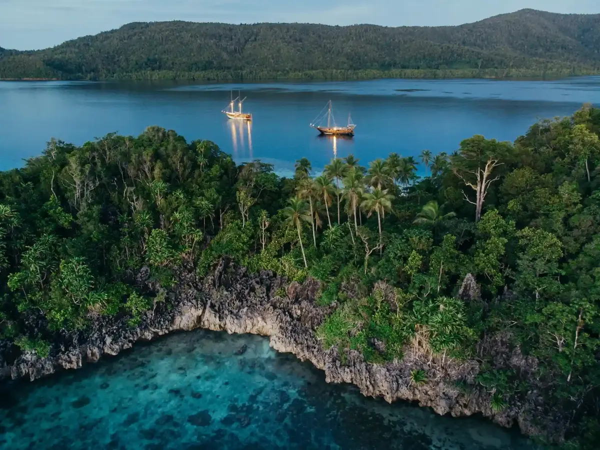 Phinisi boats anchored off a jungle island in Raja Ampat